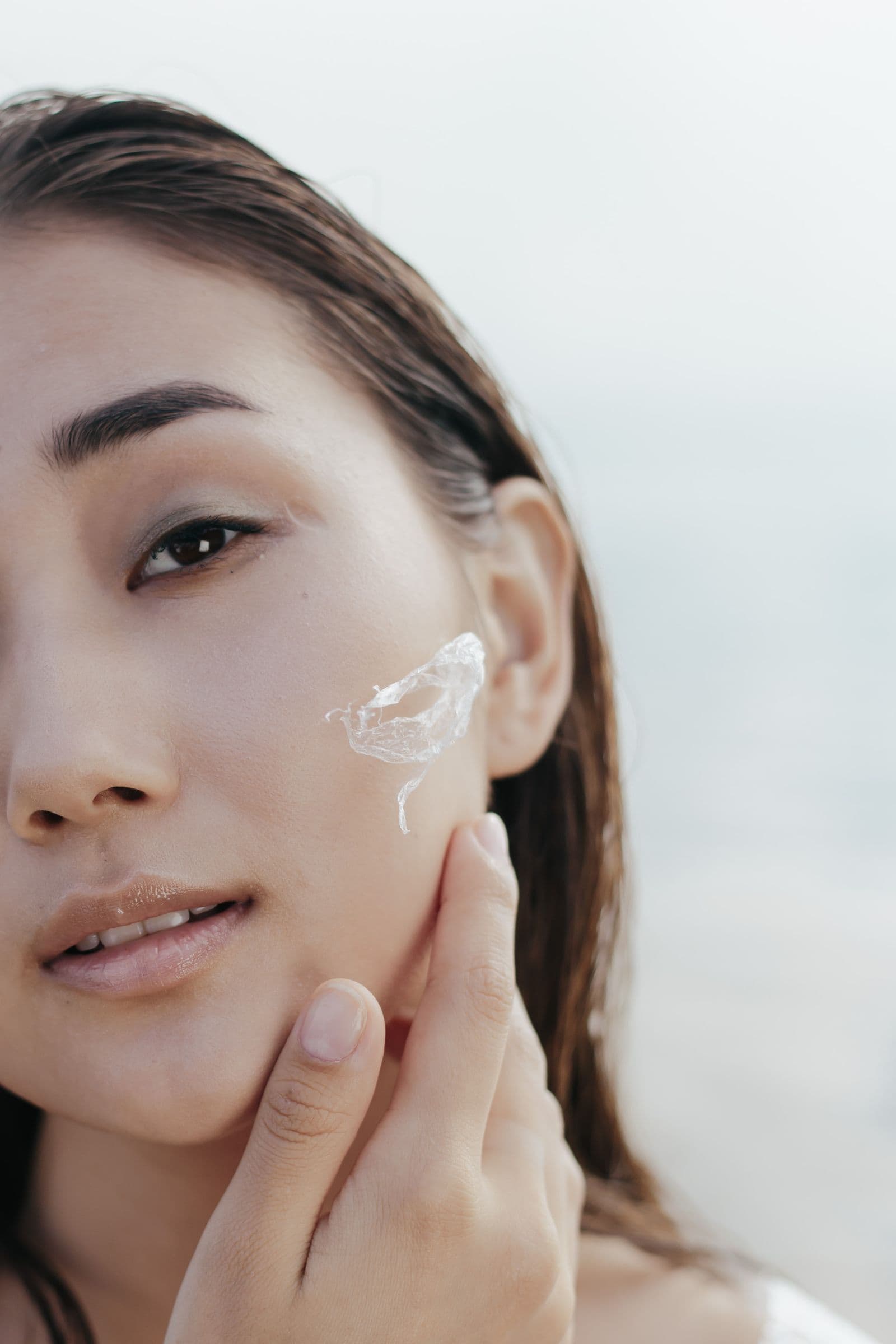 A woman with clear, healthy skin applying moisturizer in soft natural light